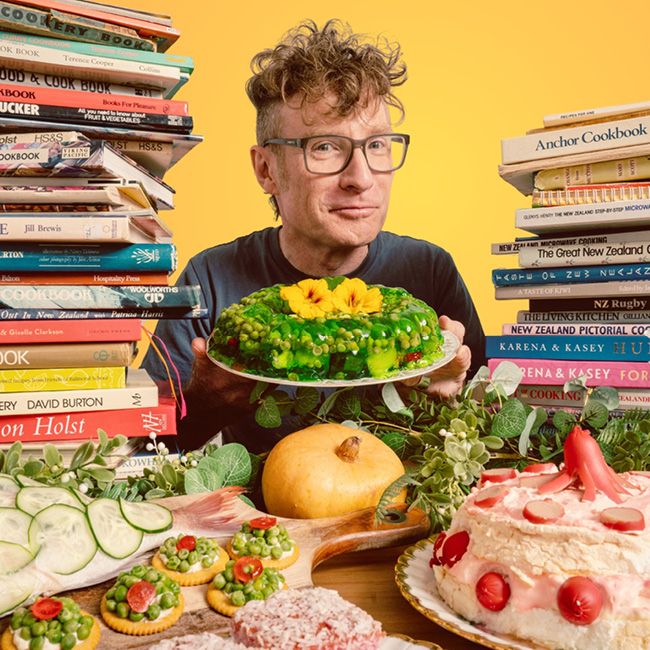 Te Radar holding plate with jelly vegetable cake surrounded by pales of cookbooks.